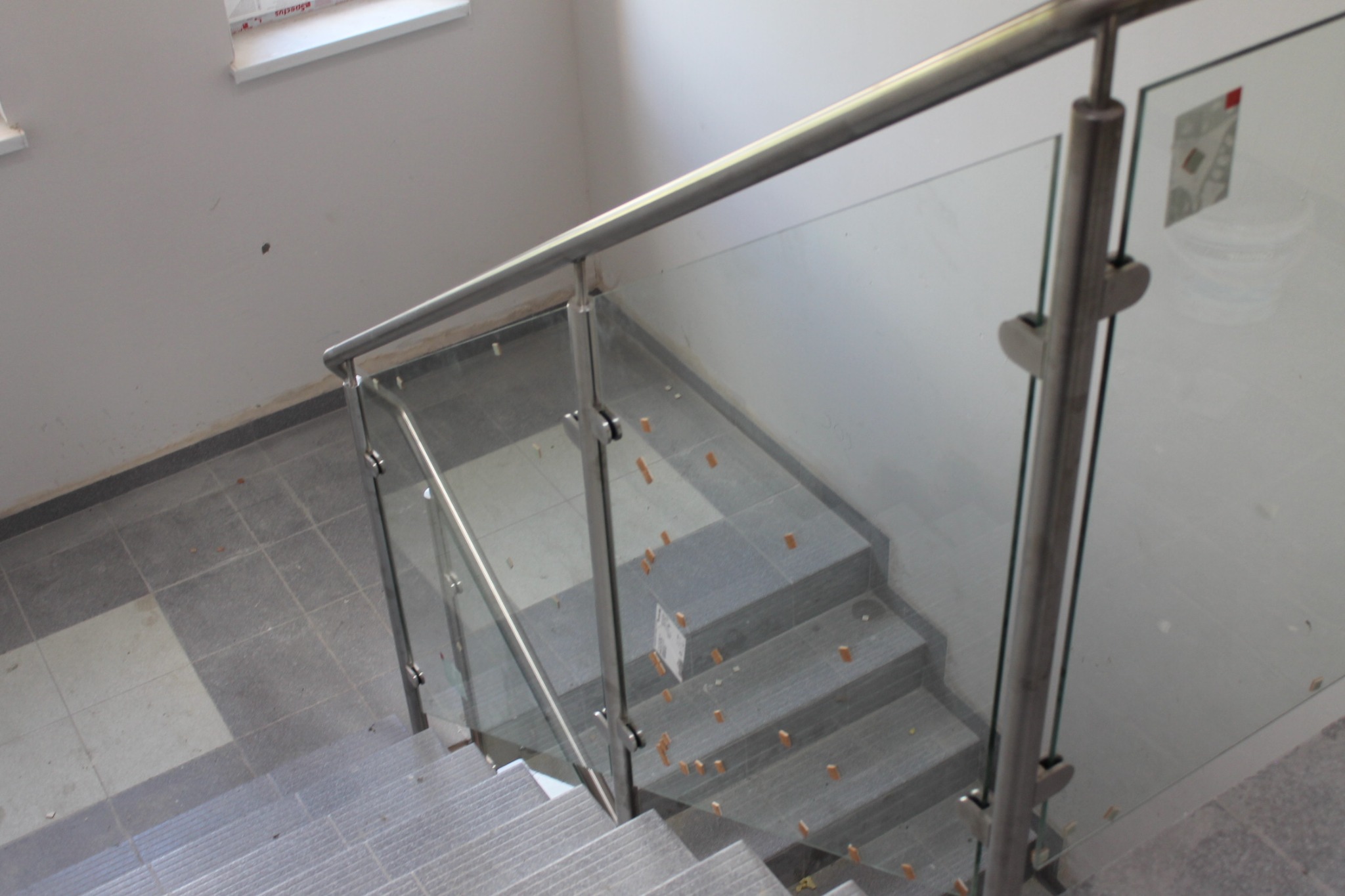 Szklana balustrada ze stalową poręczą zamontowana na schodach z szarego kamienia, widok z góry na trzy stopnie, pozostałości po montażu na stopniach.