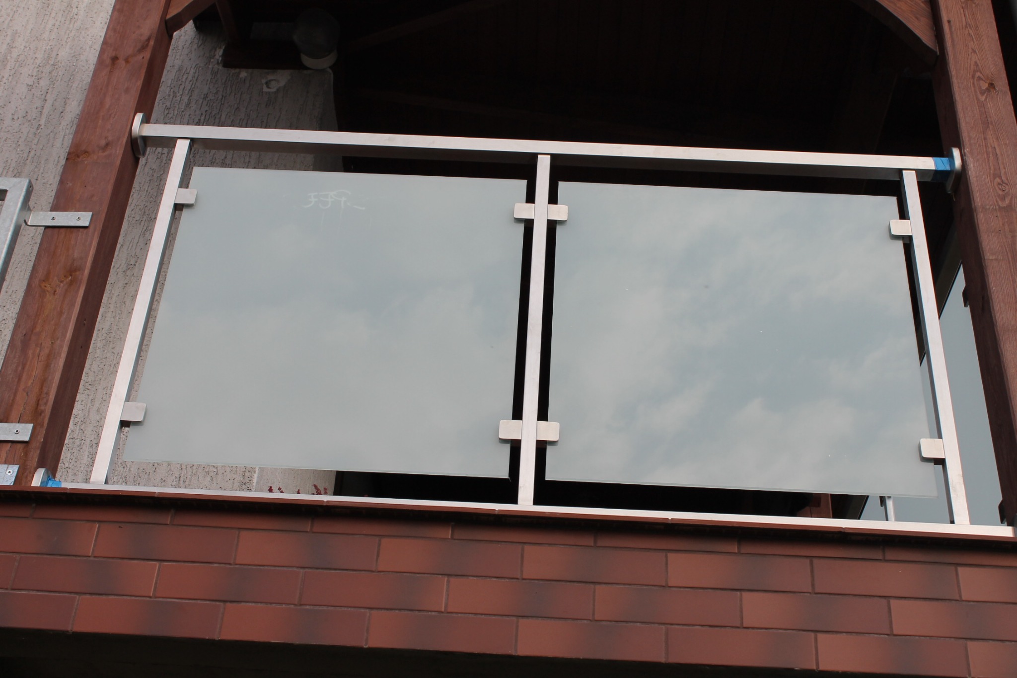 Balkon z nowoczesną szklaną balustradą z nierdzewnymi elementami mocującymi, widok z dołu na ceglany mur.