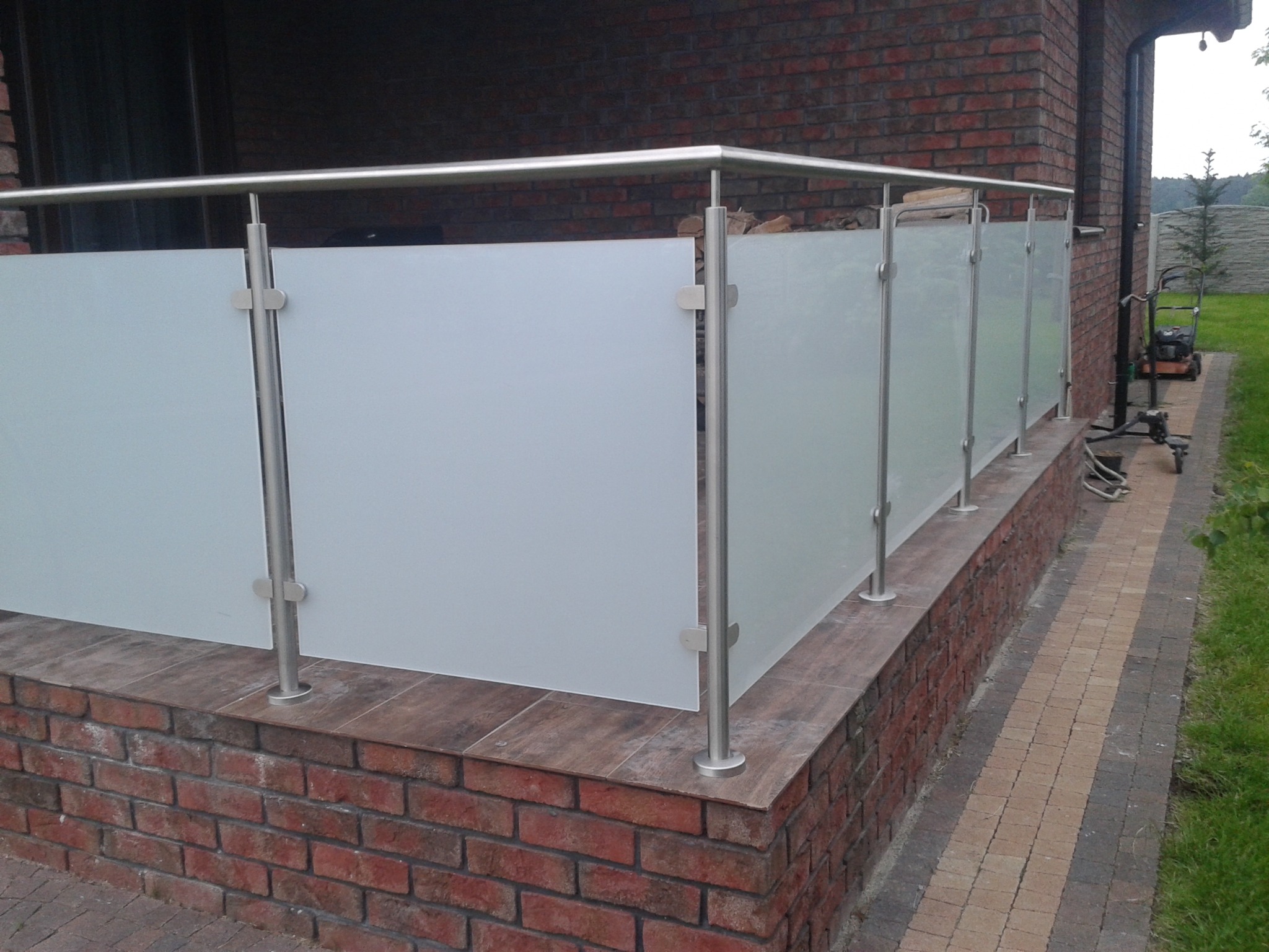 Balkon w Bonikowie z nowoczesną balustradą ze szkła matowego i stali nierdzewnej, zamontowaną na murku z cegły klinkierowej.