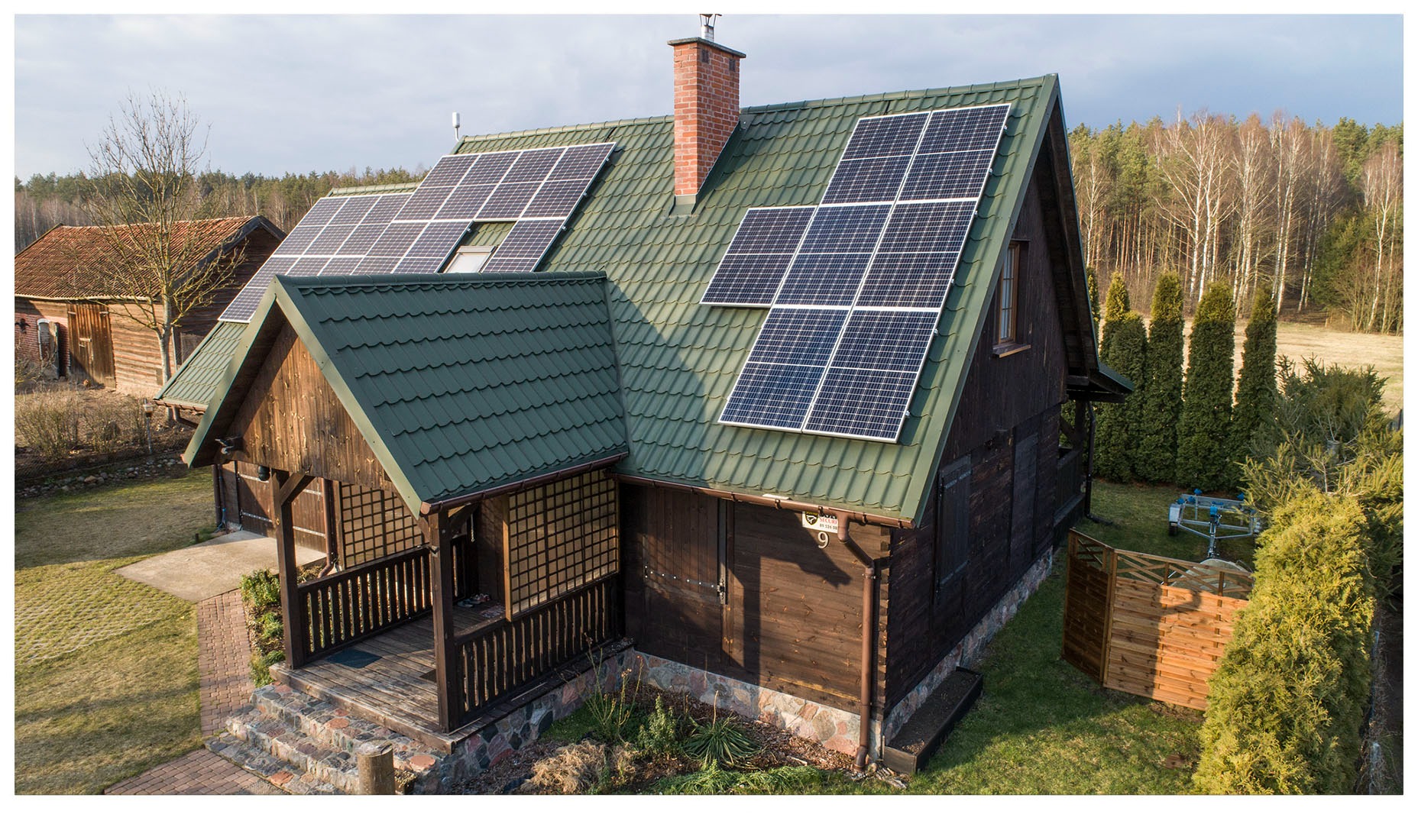 Drewniany dom z zielonym dachem i panelami słonecznymi, widok z góry, w tle las.