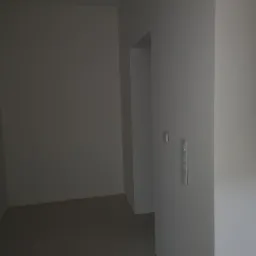 Wnętrze po nałożeniu gładzi, widoczne gładkie, szare ściany i podłoga z szarych płytek, z zamontowanymi włącznikami światła.