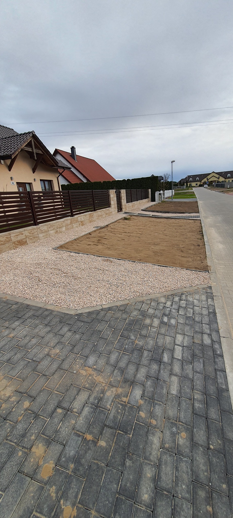 Przygotowany teren pod przyszły ogród: wyrównana ziemia, wysypany ozdobny kamień, obrzeża z kostki brukowej, w tle ogrodzenie z drewnianymi panelami.