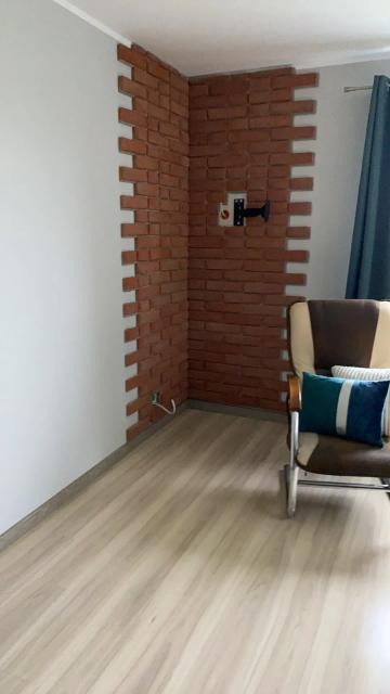 Fragment ściany wyłożony dekoracyjną cegłą w rogu pokoju, z widocznym uchwytem na telewizor, jasnymi panelami podłogowymi i fotelem z poduszką w tle.