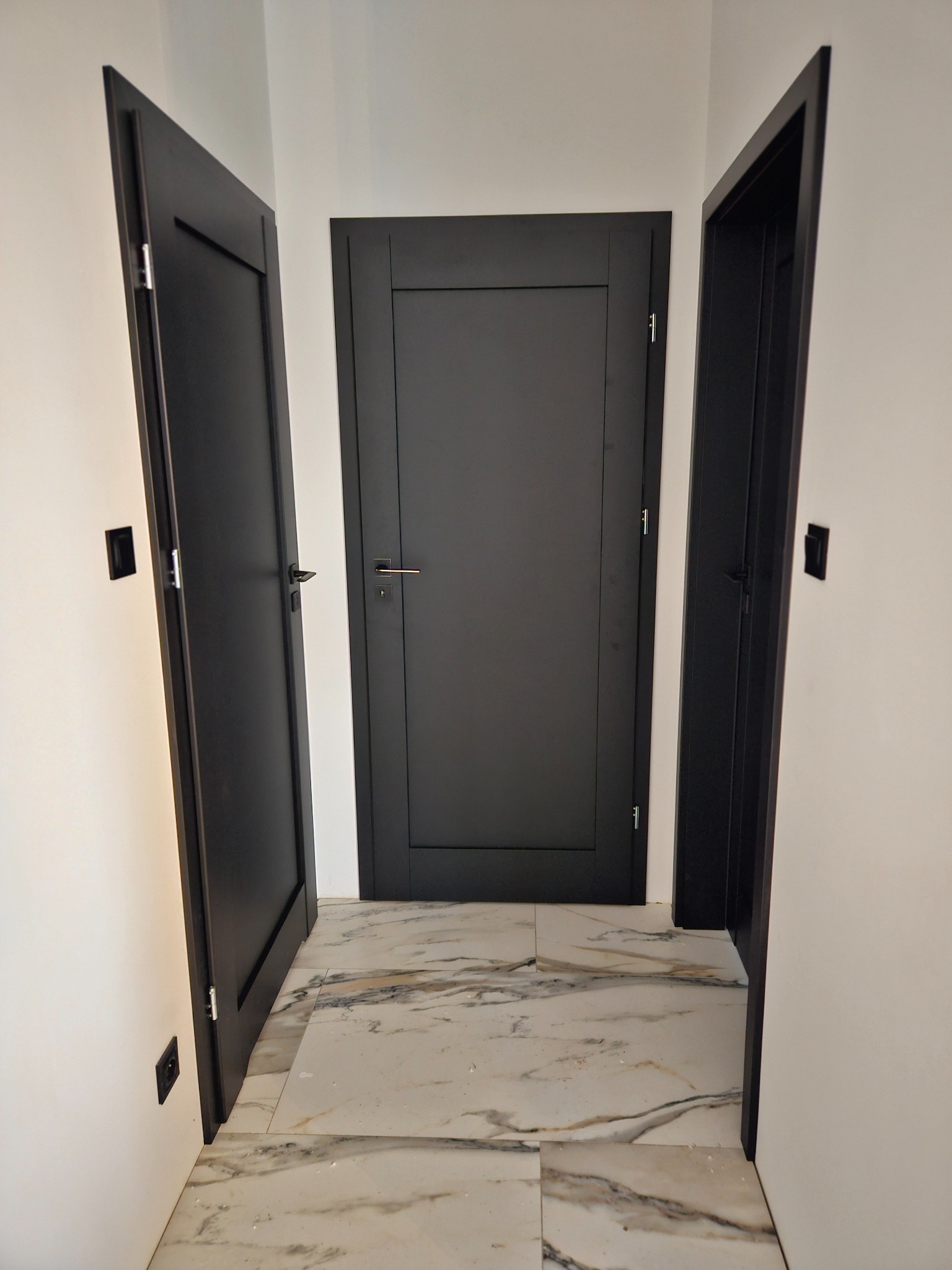 Trzy czarne, nowoczesne drzwi wewnętrzne w białym korytarzu z marmurową podłogą, widok z perspektywy podłogi.