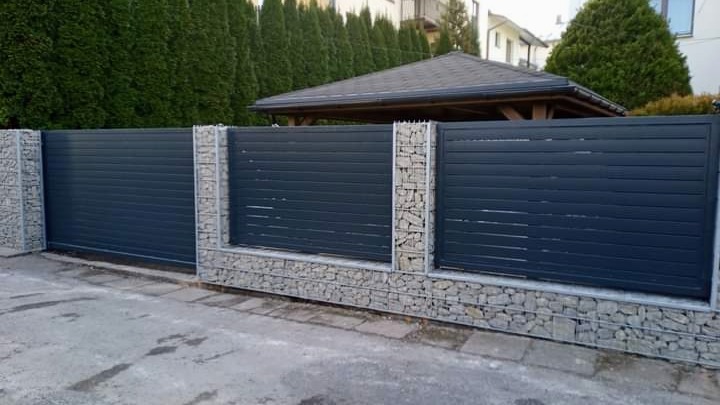 Nowoczesne ogrodzenie panelowe w kolorze grafitowym z gabionowymi słupkami i podmurówką, widok z zewnątrz posesji.