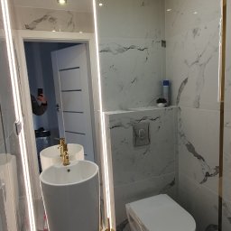 BUDAR - Nowoczesna łazienka z marmurowymi płytkami, wolnostojącą umywalką z złotą armaturą, podświetlanym lustrem i wiszącą toaletą.