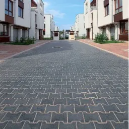 Ulica wyłożona szarą kostką brukową w kształcie litery H, pomiędzy rzędami nowoczesnych, białych domów z brązowymi elementami wykończeniowymi