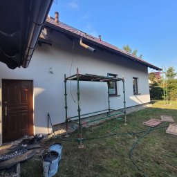 P.H.U Len-Bud - Dom jednorodzinny w Pszczółkach z jasną elewacją w trakcie prac wykończeniowych; widoczne rusztowanie, wiaderka z farbą, zabezpieczenia przy drzwiach wejściowych i przygotowane płyty chodnikowe...