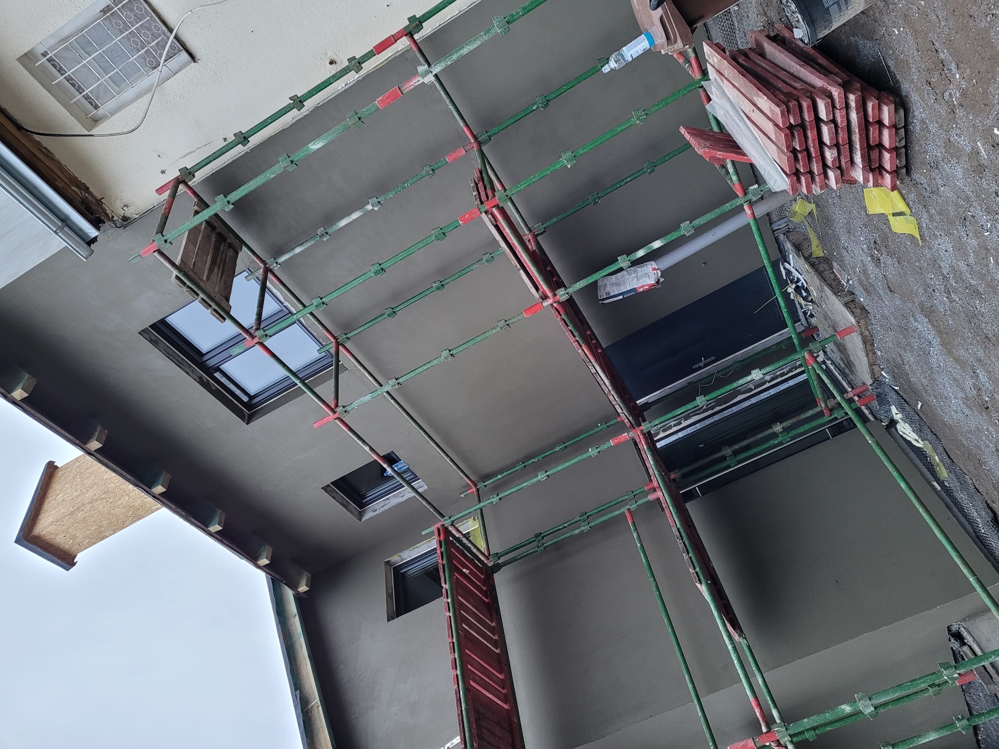 Świeżo otynkowana elewacja budynku z widocznymi rusztowaniami i oknami dachowymi, ujęcie z dołu.