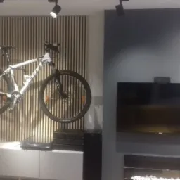 Biały rower górski zawieszony na ścianie z drewnianych listew w nowoczesnym salonie z szarą ścianą, telewizorem i kominkiem elektrycznym.