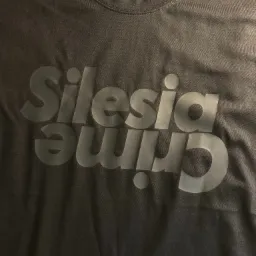 Ciemna koszulka z nadrukiem 'Silesia Crime' w odcieniach szarości, leżąca płasko, widoczny dekolt.