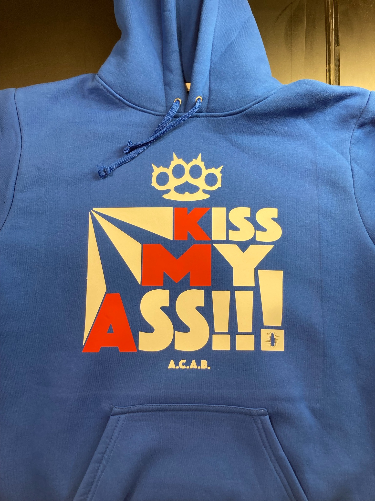 Niebieska bluza z kapturem, z nadrukiem w kolorach czerwonym, białym i żółtym przedstawiającym kastet i napis 'KISS MY ASS!!! A.C.A.B.'
