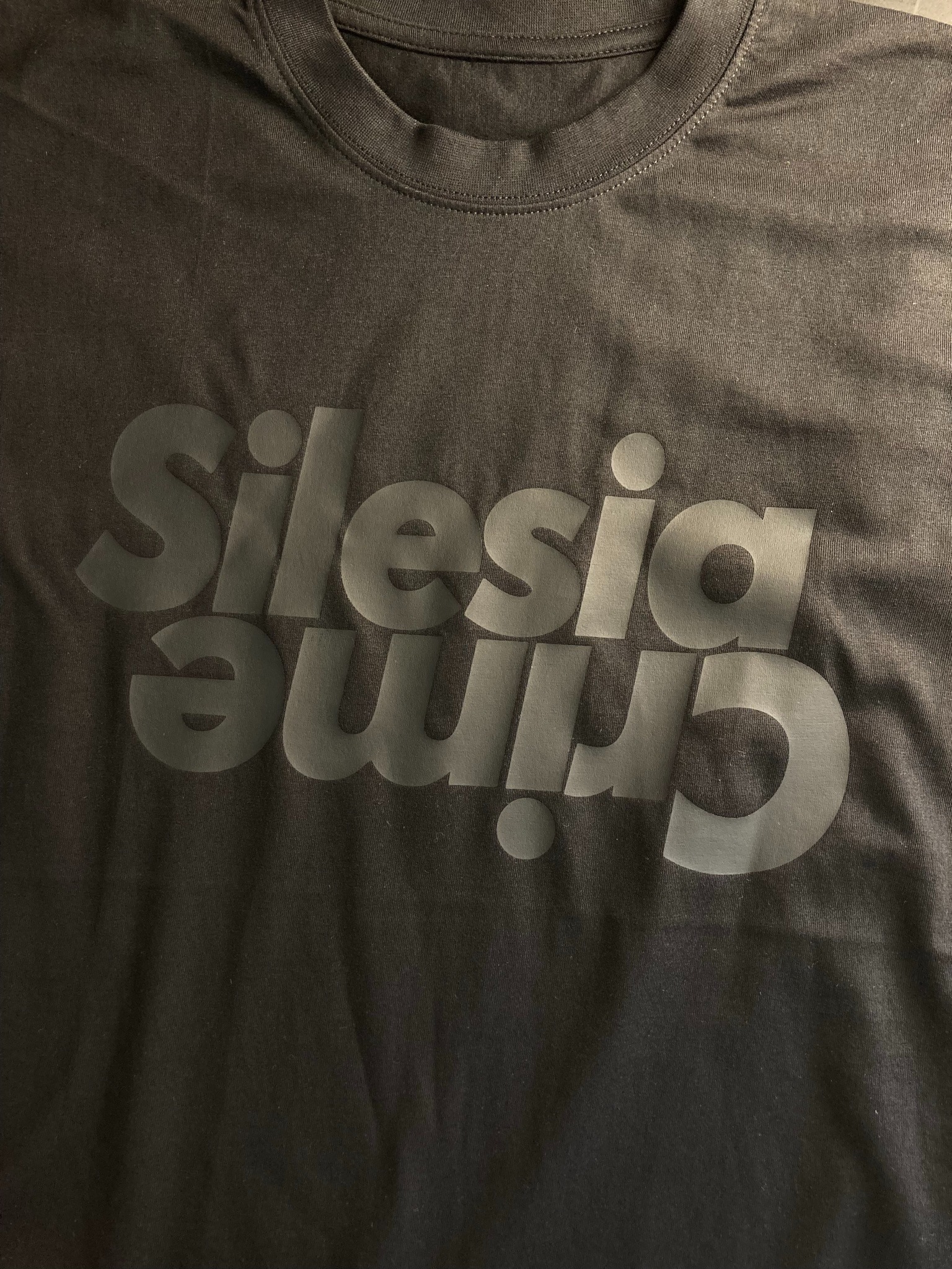 Ciemna koszulka z nadrukiem 'Silesia Crime' w odcieniach szarości, leżąca płasko, widoczny dekolt.