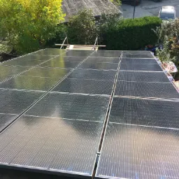 Widok z góry na panele słoneczne na dachu domu w słoneczny dzień, z widocznym otoczeniem budynku i zielenią.