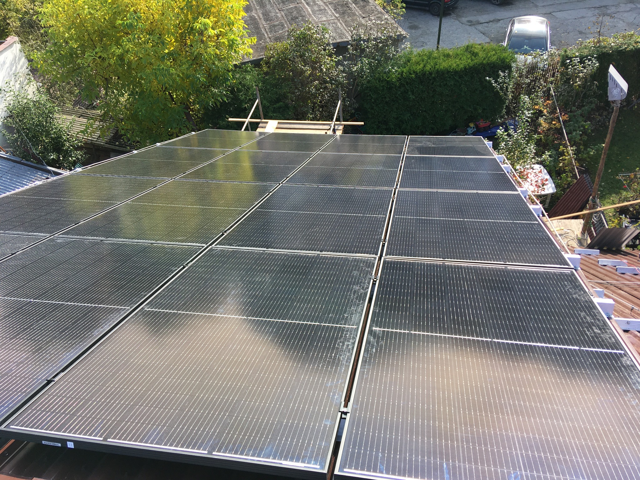 Widok z góry na panele słoneczne na dachu domu w słoneczny dzień, z widocznym otoczeniem budynku i zielenią.