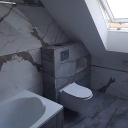 SZWAGRO-BUD - Nowoczesna łazienka na poddaszu w Limanowej z marmurowymi płytkami, wiszącą toaletą i zabudowaną spłuczką oraz wanną.