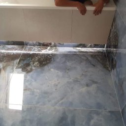 SZWAGRO-BUD - Montaż wanny w łazience z niebiesko-brązową marmurkową glazurą na podłodze i ścianach, widoczne otwory na instalacje wodne.