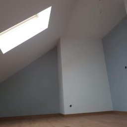 SZWAGRO-BUD - Pomalowane na szaro i biało poddasze ze skośnym sufitem i oknem dachowym, widoczne ślady po gniazdkach elektrycznych.