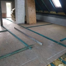 SZWAGRO-BUD - Poddasze w trakcie ocieplania: widoczne płyty OSB, wełna mineralna między legarami, okno dachowe, fragment ściany z betonu komórkowego i cegły.