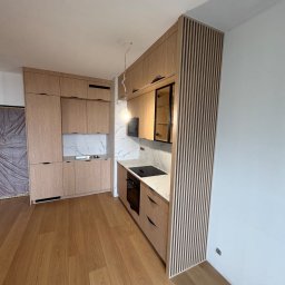 Meble Zbyszek - Jasna kuchnia z drewnianymi frontami i marmurowym blatem. Zabudowa kuchenna z pionowymi lamelami. Nowoczesny design z oświetleniem punktowym.