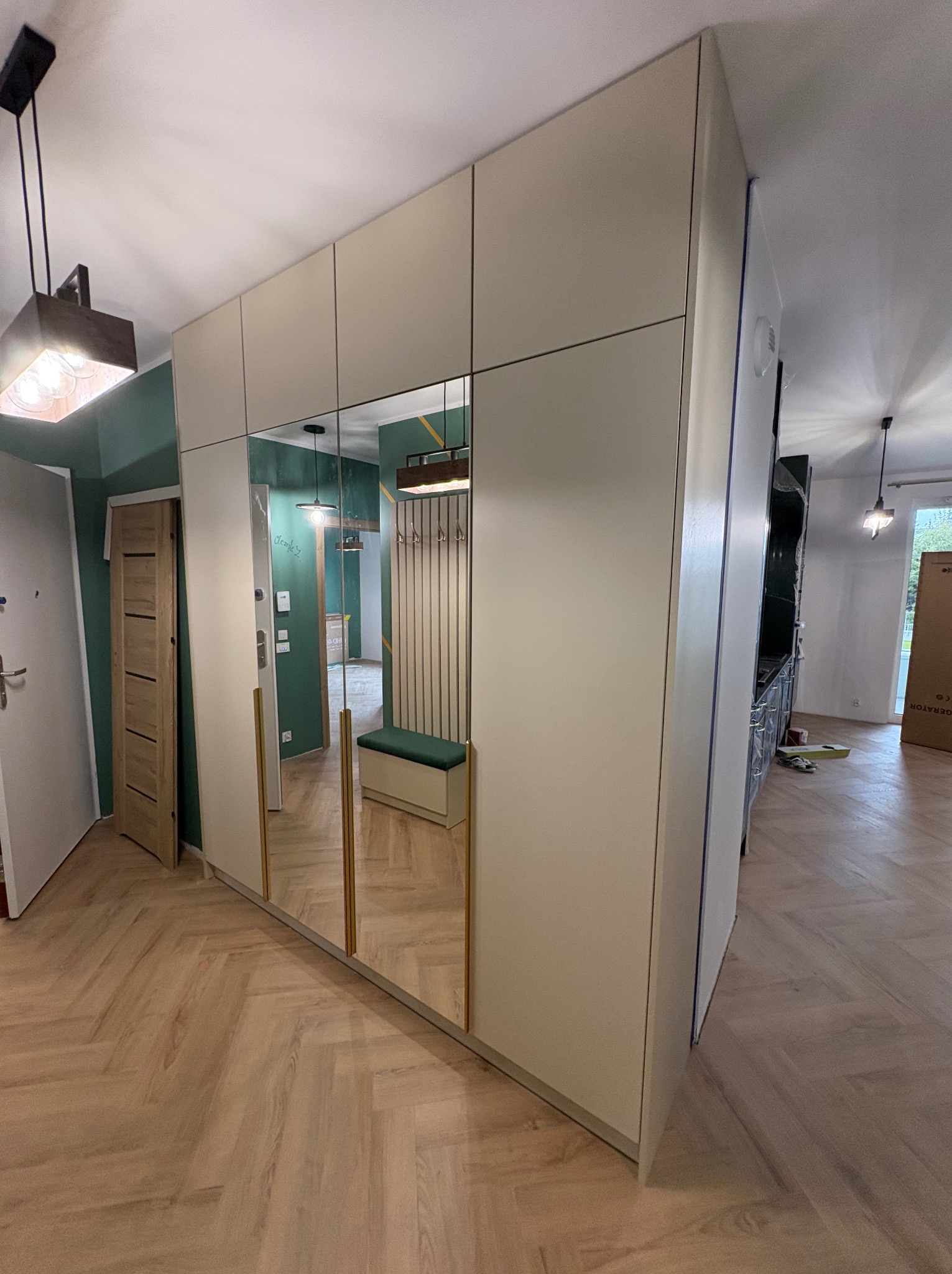 Jasna szafa wnękowa z lustrami w przedpokoju, odbicie wnętrza z wieszakiem i siedziskiem. Parkiet w jodełkę, lampa wisząca.