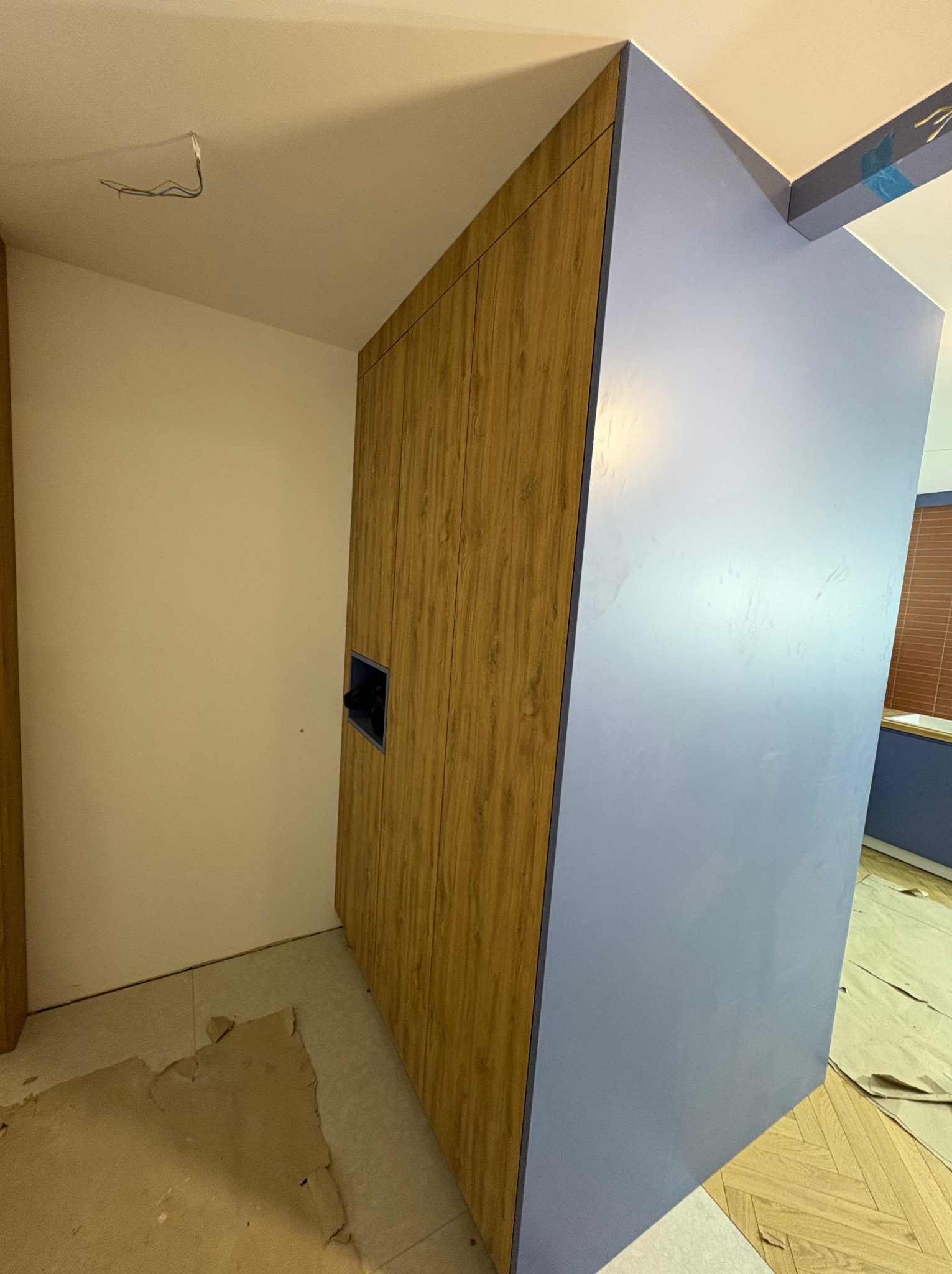 Wnętrze z szafą wnękową: fronty z drewnopodobnym dekorem i boki w odcieniach fioletu. Widoczne niedokończone wykończenie podłogi i wystające kable z sufitu.