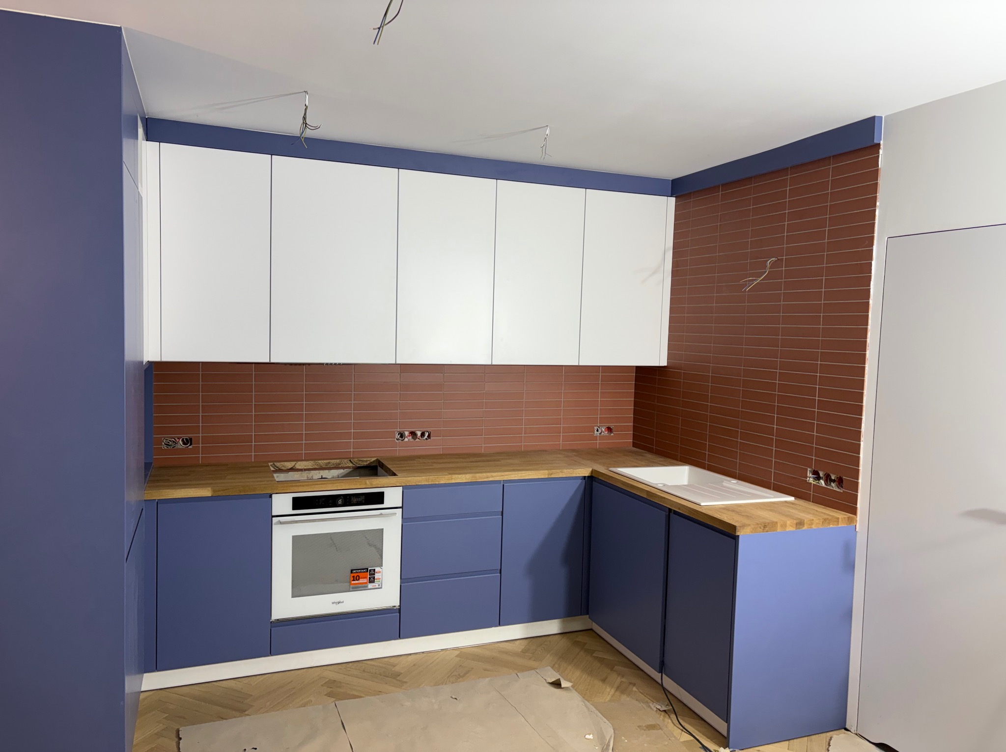 Niebiesko-biała kuchnia na wymiar z drewnianym blatem i ceglaną ścianą w Radomsku. Widoczne niedokończone prace wykończeniowe.