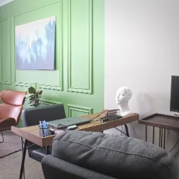 Gabinet z biurkiem, laptopem, manekinem głowy z elektrodami EEG, krzesłem i obrazem górskiego lasu we mgle na ścianie.