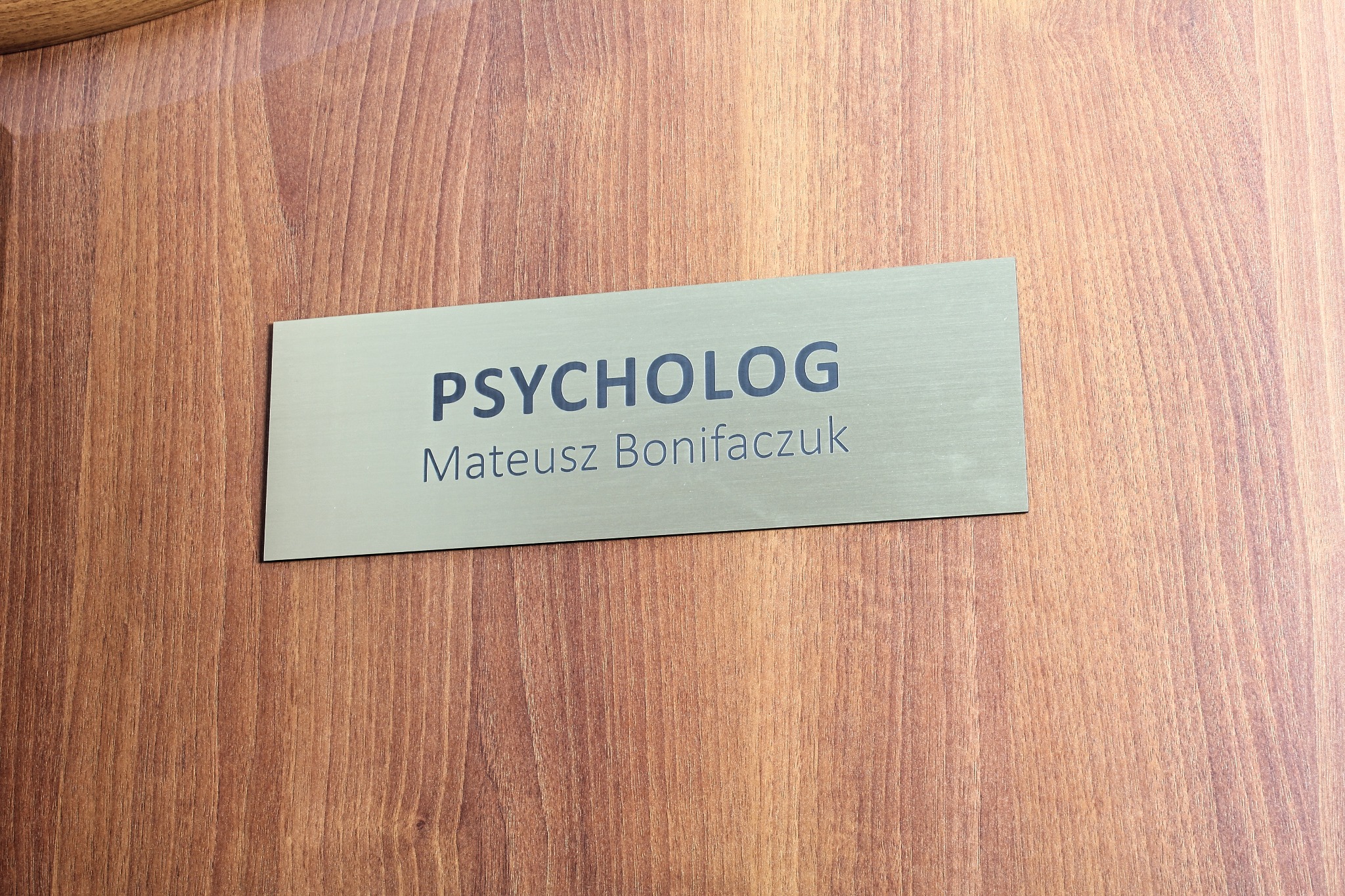 Tabliczka na drzwiach gabinetu z napisem 'PSYCHOLOG Mateusz Bonifaczuk' na tle drewnianej powierzchni.