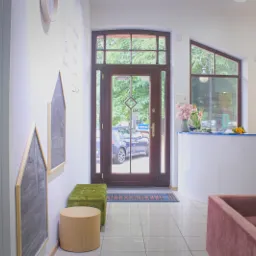 Jasne wnętrze gabinetu z recepcją, kwiatami i elementami dekoracyjnymi w kształcie domków na ścianie.