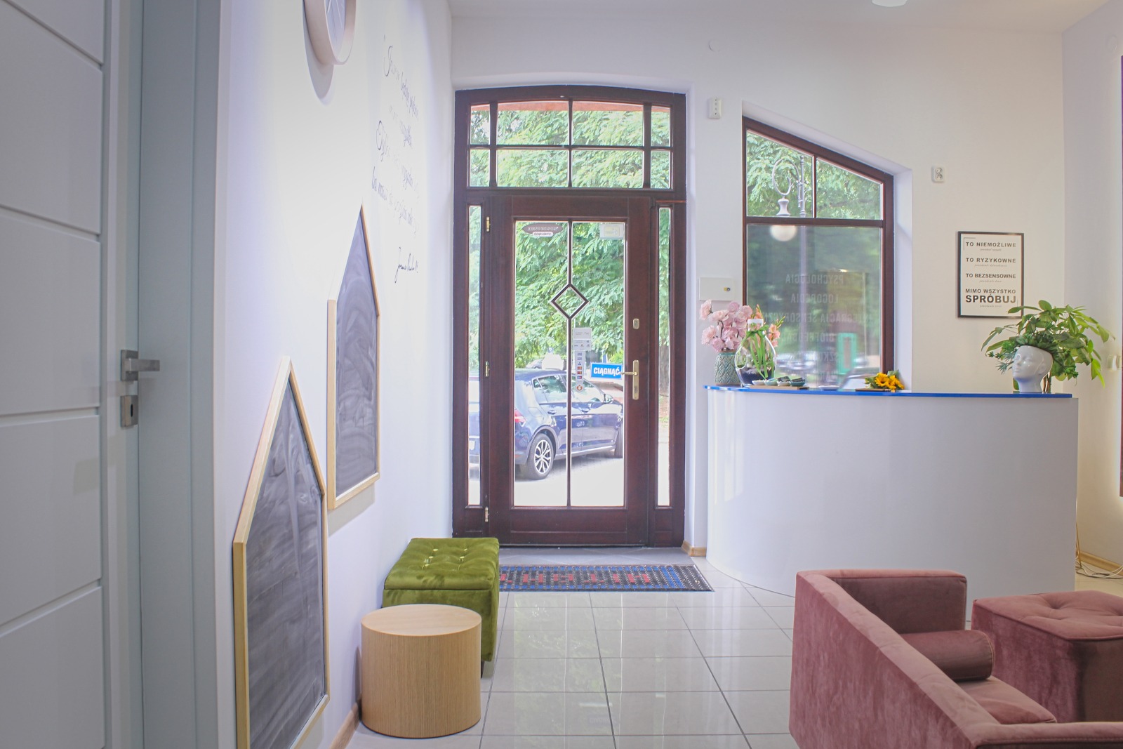Jasne wnętrze gabinetu z recepcją, kwiatami i elementami dekoracyjnymi w kształcie domków na ścianie.