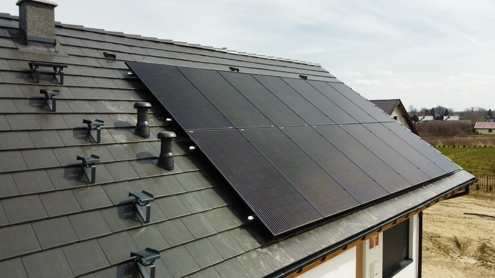 Panele słoneczne na dachu domu jednorodzinnego z szarej dachówki, widoczne elementy montażowe i komin