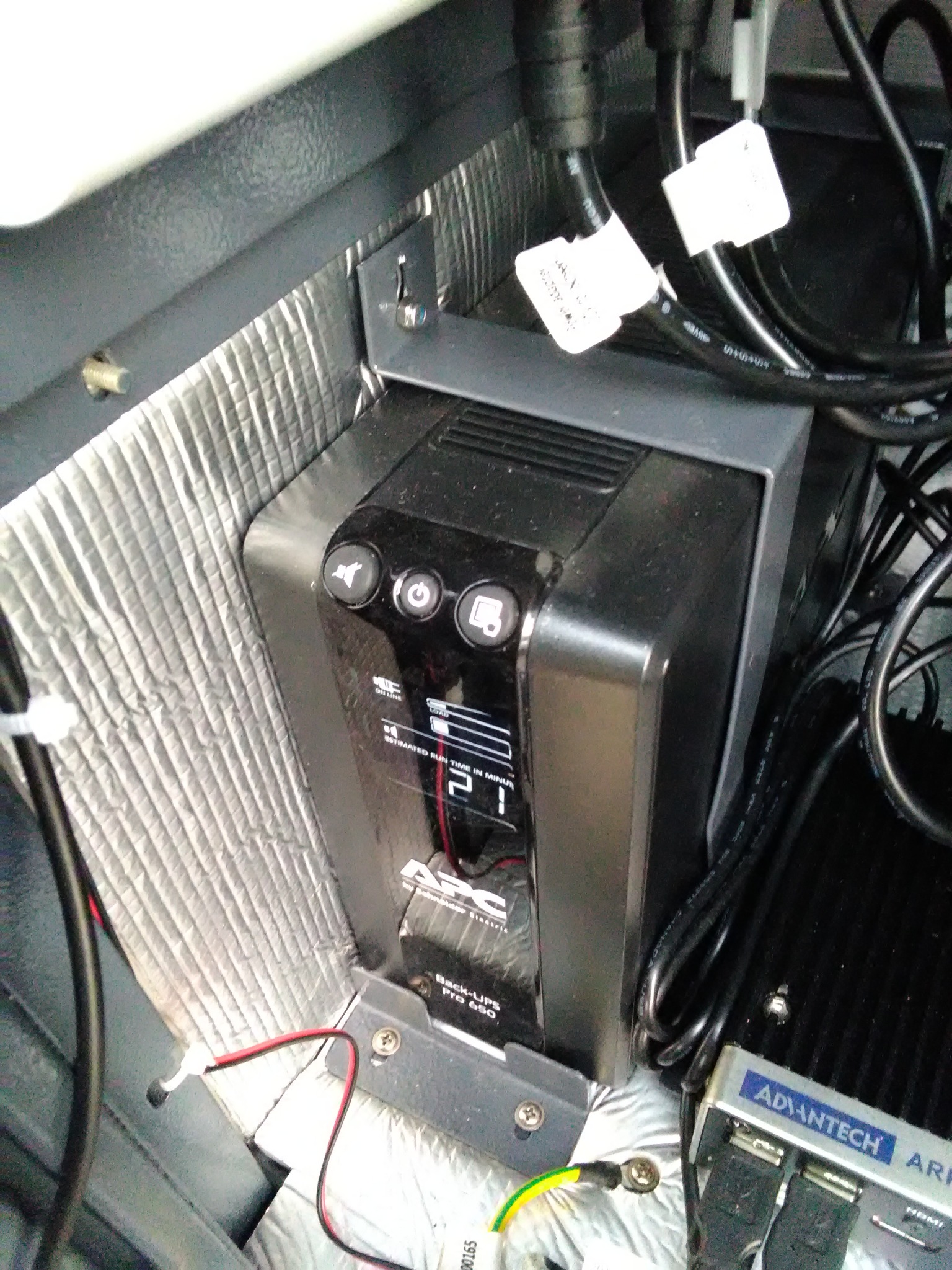 Zamontowany zasilacz awaryjny UPS Back-UPS Pro 650 firmy APC w metalowej obudowie, widoczne kable zasilające i przewody, izolacja termiczna w tle.