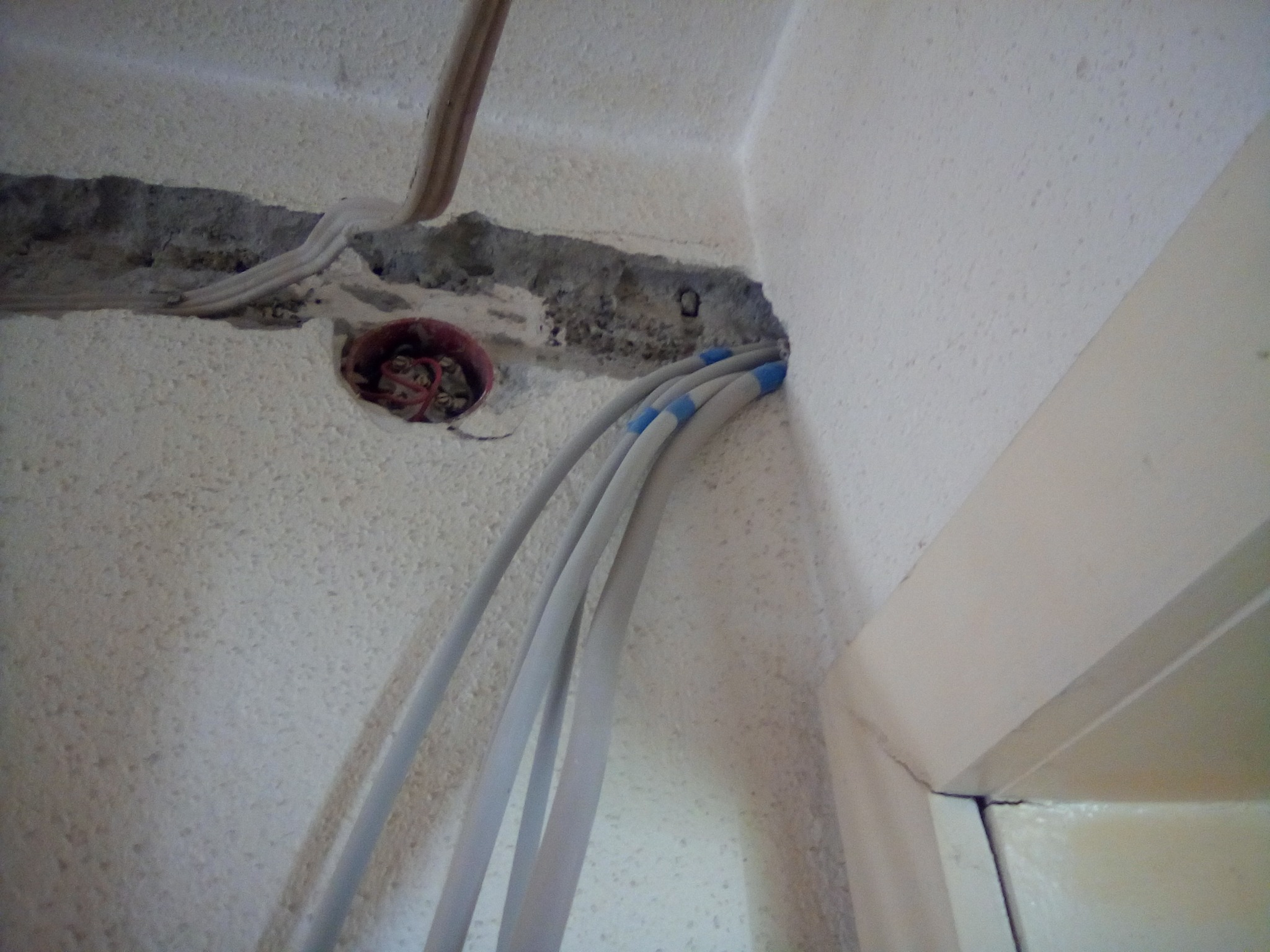 Wprowadzenie kabli elektrycznych w ścianę z widoczną puszką instalacyjną i bruzdą w ścianie, zabezpieczone końcówki kabli.