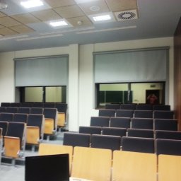 Przedsiębiorstwo Usługowo Handlowo Produkcyjne EUROL Małgorzata Czarnotta - Wnętrze sali wykładowej z rzędami krzeseł i opuszczonymi szarymi roletami w oknach, widoczna osoba w odbiciu okna.