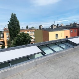 Przedsiębiorstwo Usługowo Handlowo Produkcyjne EUROL Małgorzata Czarnotta - Widok z dachu na budynki w tle, na pierwszym planie okna dachowe z zamontowanymi osłonami przeciwsłonecznymi w kolorze białym.