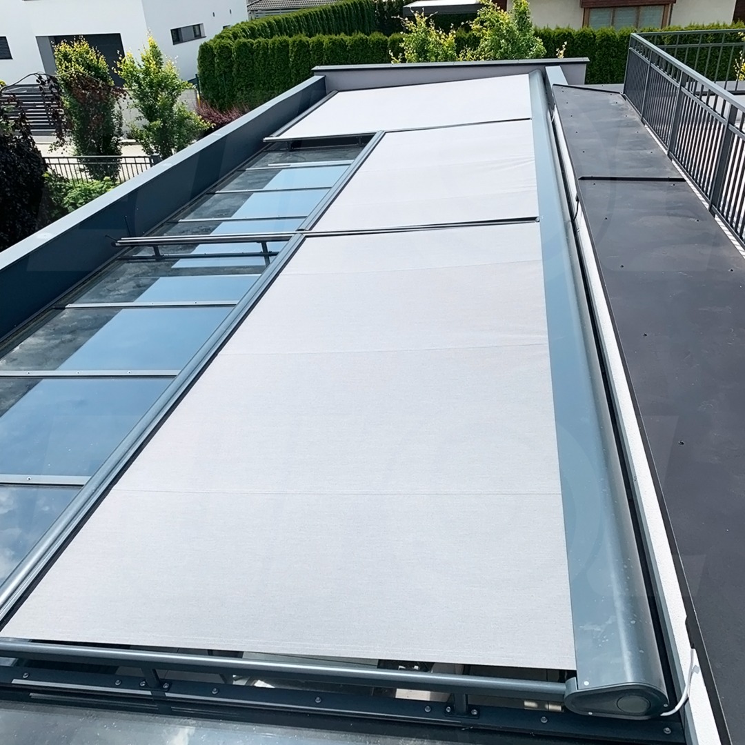Zewnętrzna, jasnoszara osłona przeciwsłoneczna zamontowana na szklanym dachu tarasu, widok z góry, nowoczesne budownictwo.