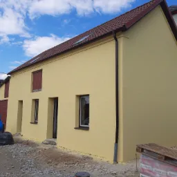 Żółta elewacja budynku po nałożeniu tynku strukturalnego, widoczne worki z resztkami materiałów budowlanych i paleta z zapasem tynku.