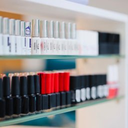 ESTETYKA Centrum Kosmetologii i Medycyny Estetycznej - Półki w salonie z rzędami lakierów do paznokci w odcieniach bieli, czerni i czerwieni, niektóre z srebrnymi nakrętkami, inne z czarnymi i czerwonymi, z bliska widoczne etykiety produktów.