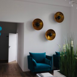 ESTETYKA Centrum Kosmetologii i Medycyny Estetycznej - Wnętrze salonu w Nakle nad Notecią z turkusowymi fotelami, złotymi dekoracjami ściennymi, roślinami ozdobnymi i niebieskimi balonami, tworzące elegancką przestrzeń.
