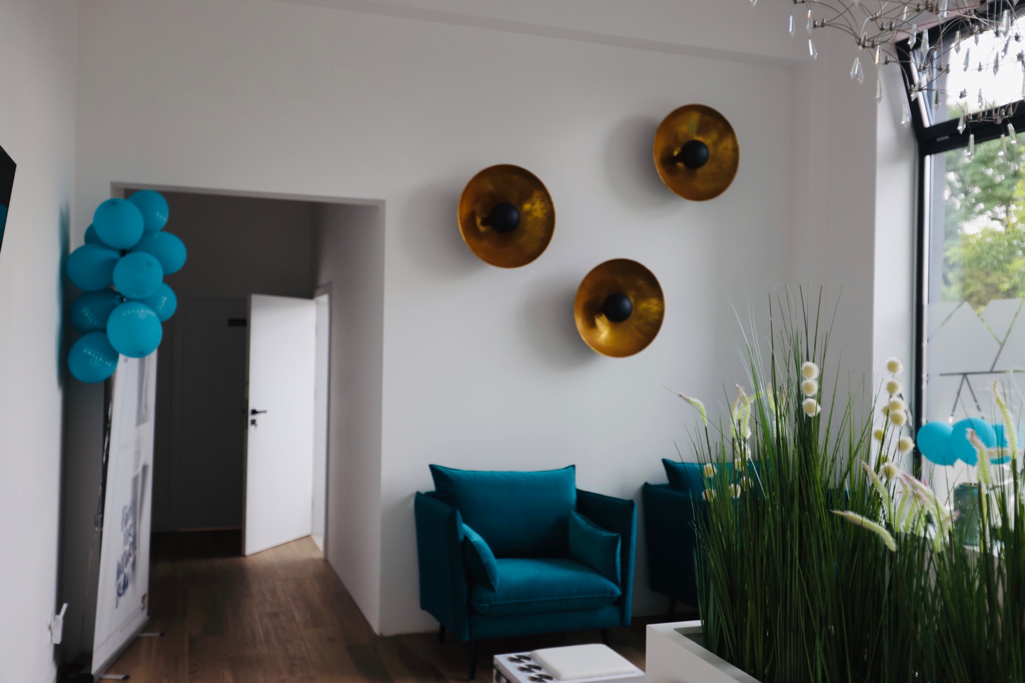 Wnętrze salonu w Nakle nad Notecią z turkusowymi fotelami, złotymi dekoracjami ściennymi, roślinami ozdobnymi i niebieskimi balonami, tworzące elegancką przestrzeń.