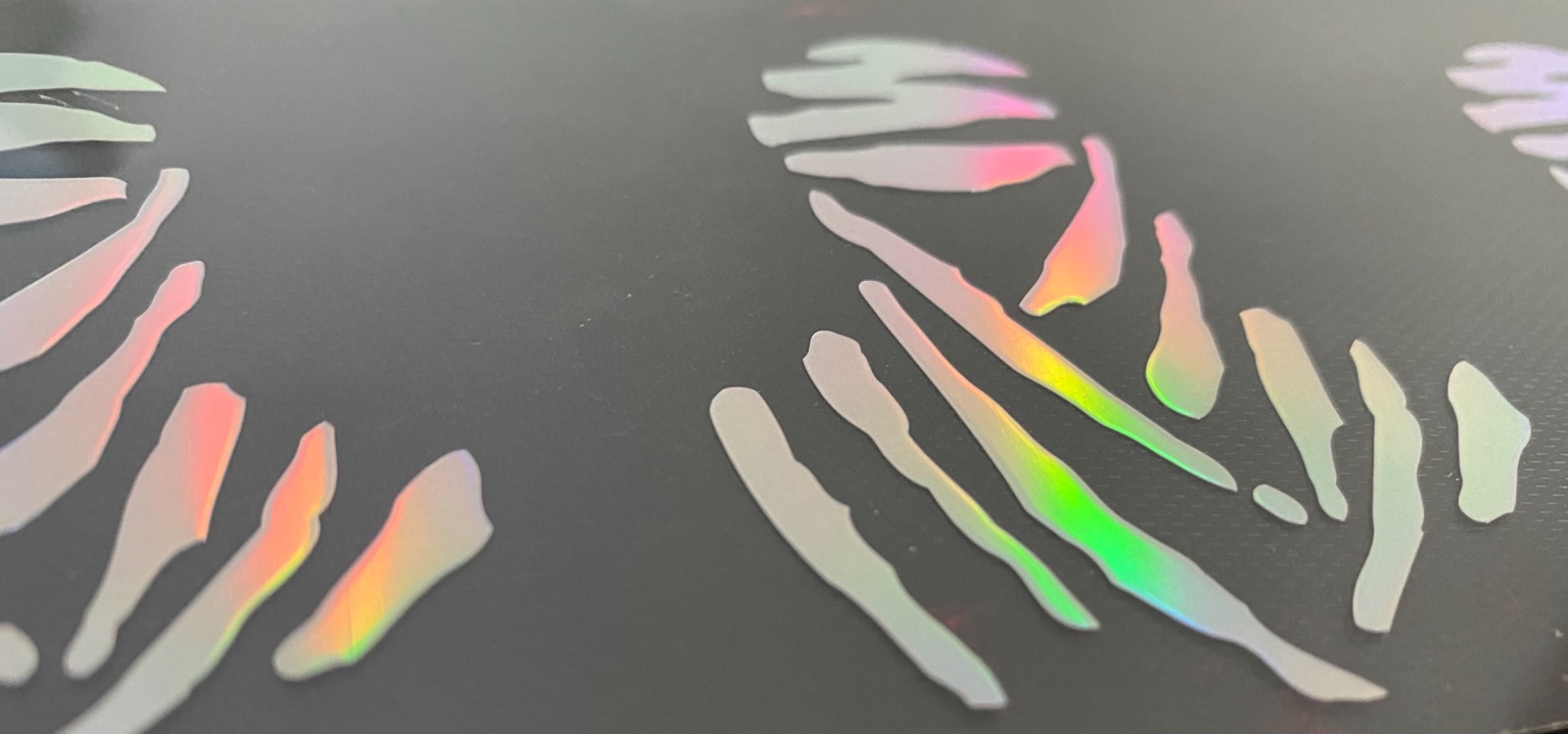 Zbliżenie holograficznych naklejek z wzorem zebry na czarnym tle, z widocznymi tęczowymi refleksami.