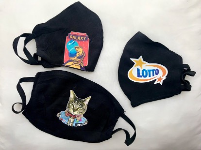 Trzy czarne maseczki ochronne z różnymi aplikacjami: astronauta Galaxy, kot w ubranku i logo Lotto, leżące na białym tle.
