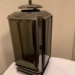 Metalowa latarnia w stylu art deco z przyciemnianymi szybami i dekoracyjnym zwieńczeniem na białym blacie.