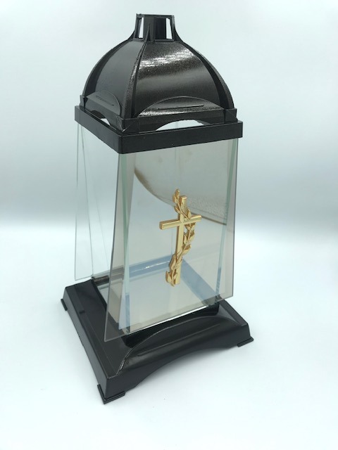 Znicz szklany z czarną podstawą i daszkiem, dekorowany złotym krzyżem z motywem roślinnym.