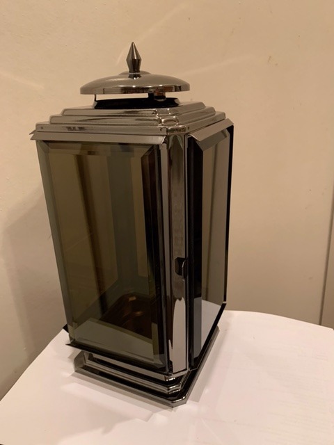 Metalowa latarnia w stylu art deco z przyciemnianymi szybami i dekoracyjnym zwieńczeniem na białym blacie.