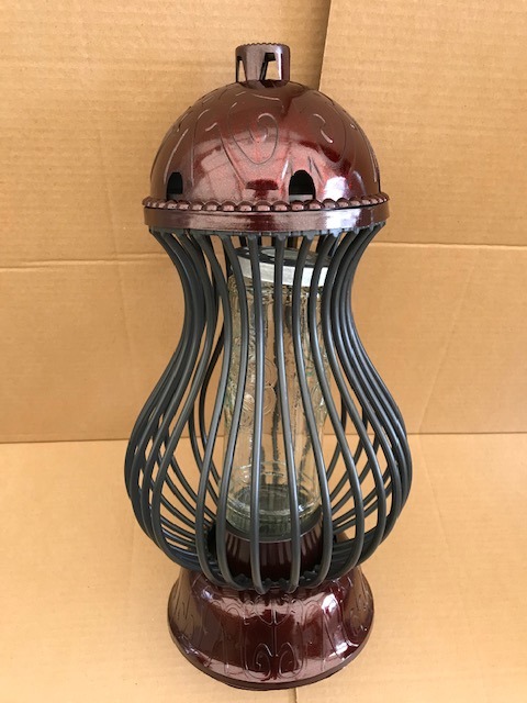 Ozdobny znicz w odcieniach brązu z metalową konstrukcją i szklanym wkładem, na tle kartonowym.