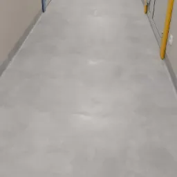 Długi korytarz z szarą, gładką podłogą, jasnymi ścianami i drzwiami z kolorowymi obramowaniami. Widok w perspektywie, z datą i godziną w prawym dolnym rogu.