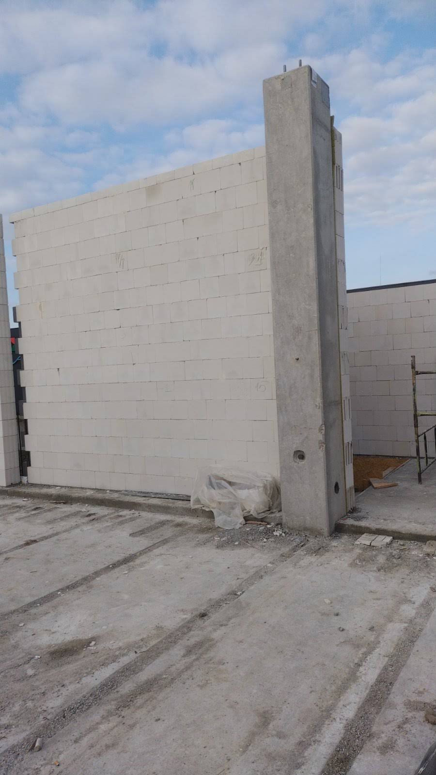 Wznoszenie ściany z betonu komórkowego Ytong z betonowym słupem wzmacniającym, widok z dołu, na zewnątrz. Ściana w surowym stanie, w trakcie budowy.