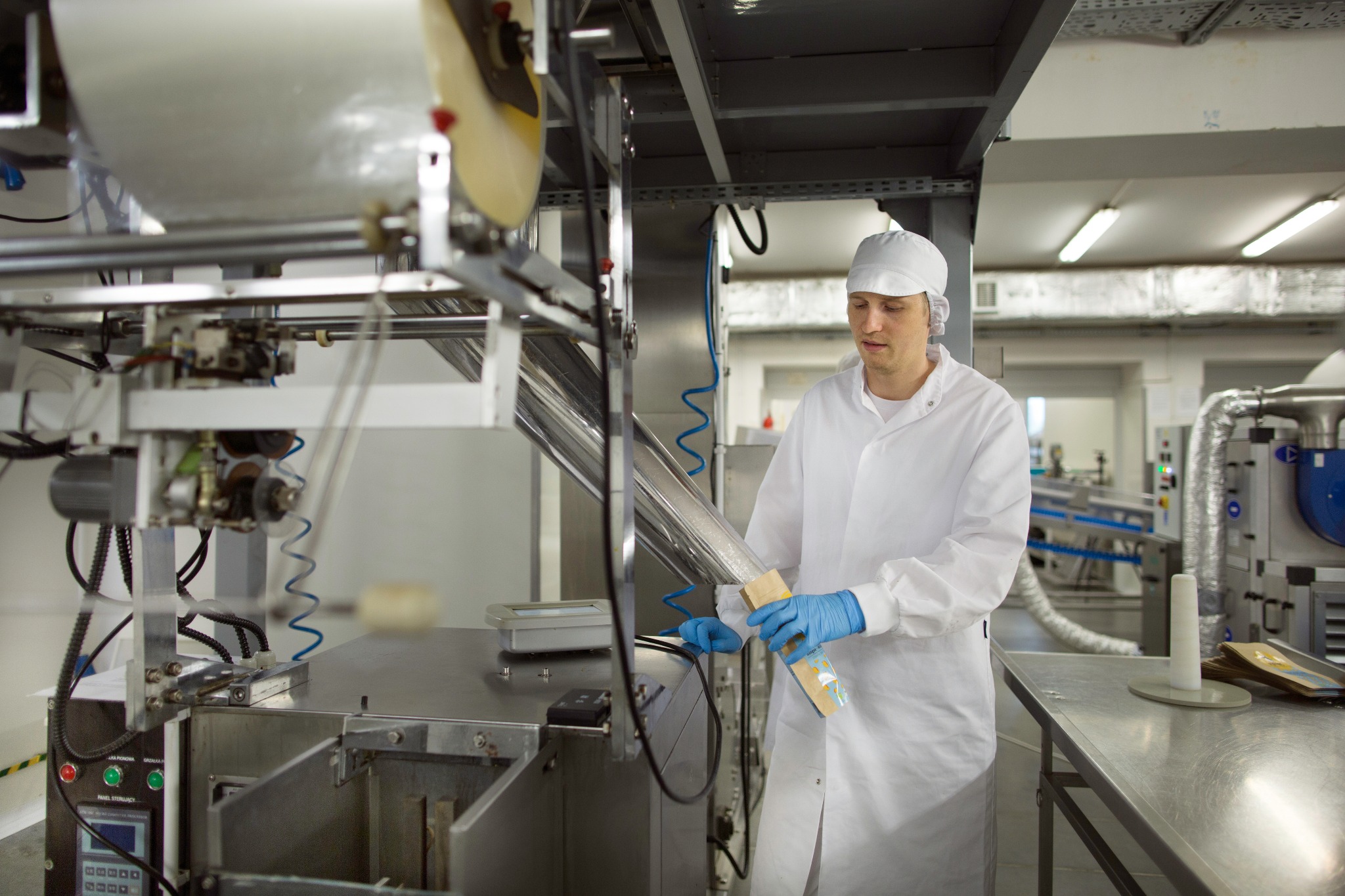 Pracownik w kombinezonie ochronnym i niebieskich rękawicach umieszcza zapakowany produkt w maszynie do pakowania w sterylnym pomieszczeniu produkcyjnym.